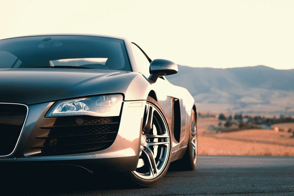 A silver sports car parked on a road with mountains in the distance