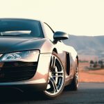 A silver sports car parked on a road with mountains in the distance